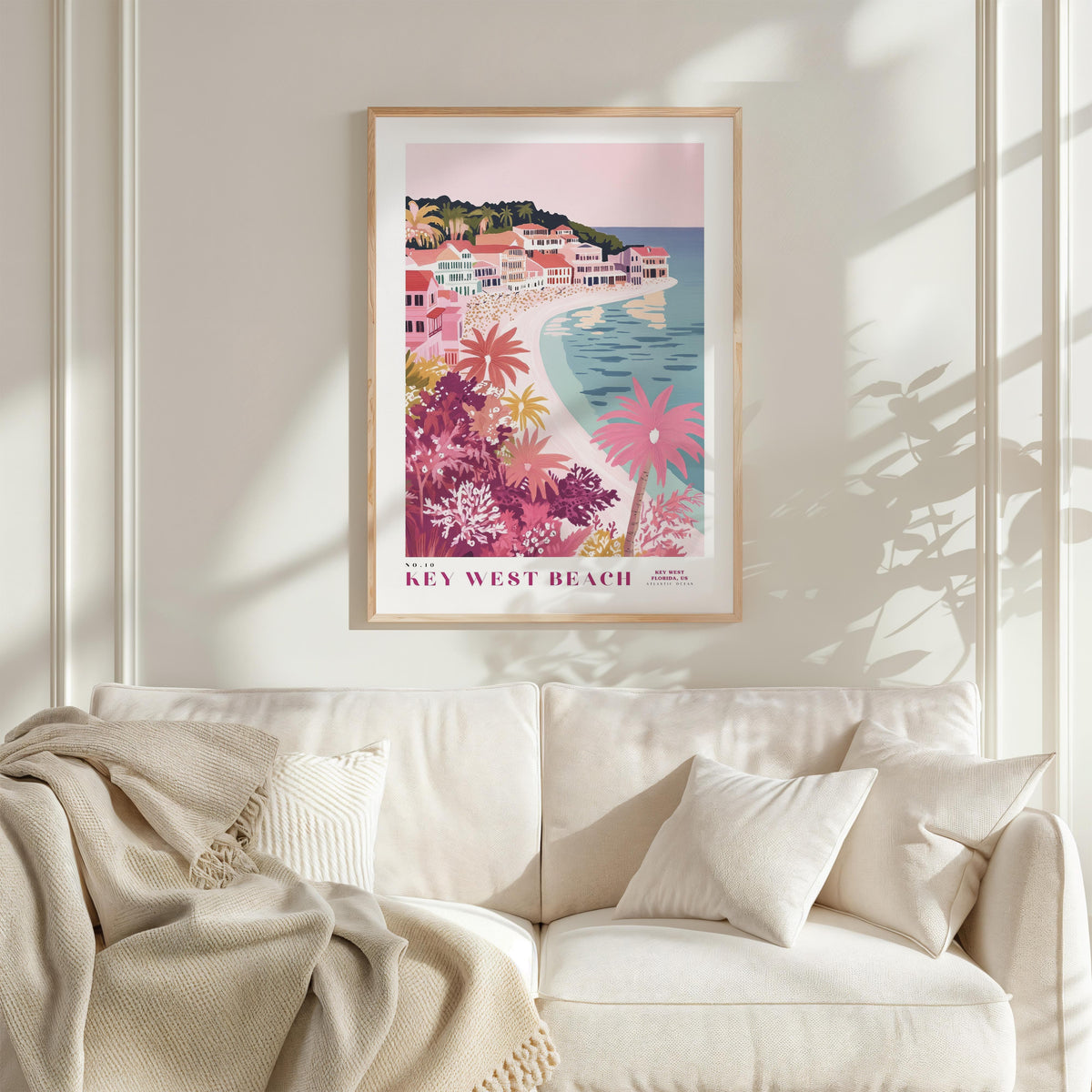 a framed poster of a beach scene with palm trees and colorful buildings, hanging on a wall above a white couch with pillows.