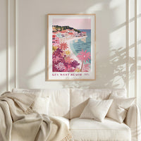 a framed poster of a beach scene with palm trees and colorful buildings, hanging on a wall above a white couch with pillows.