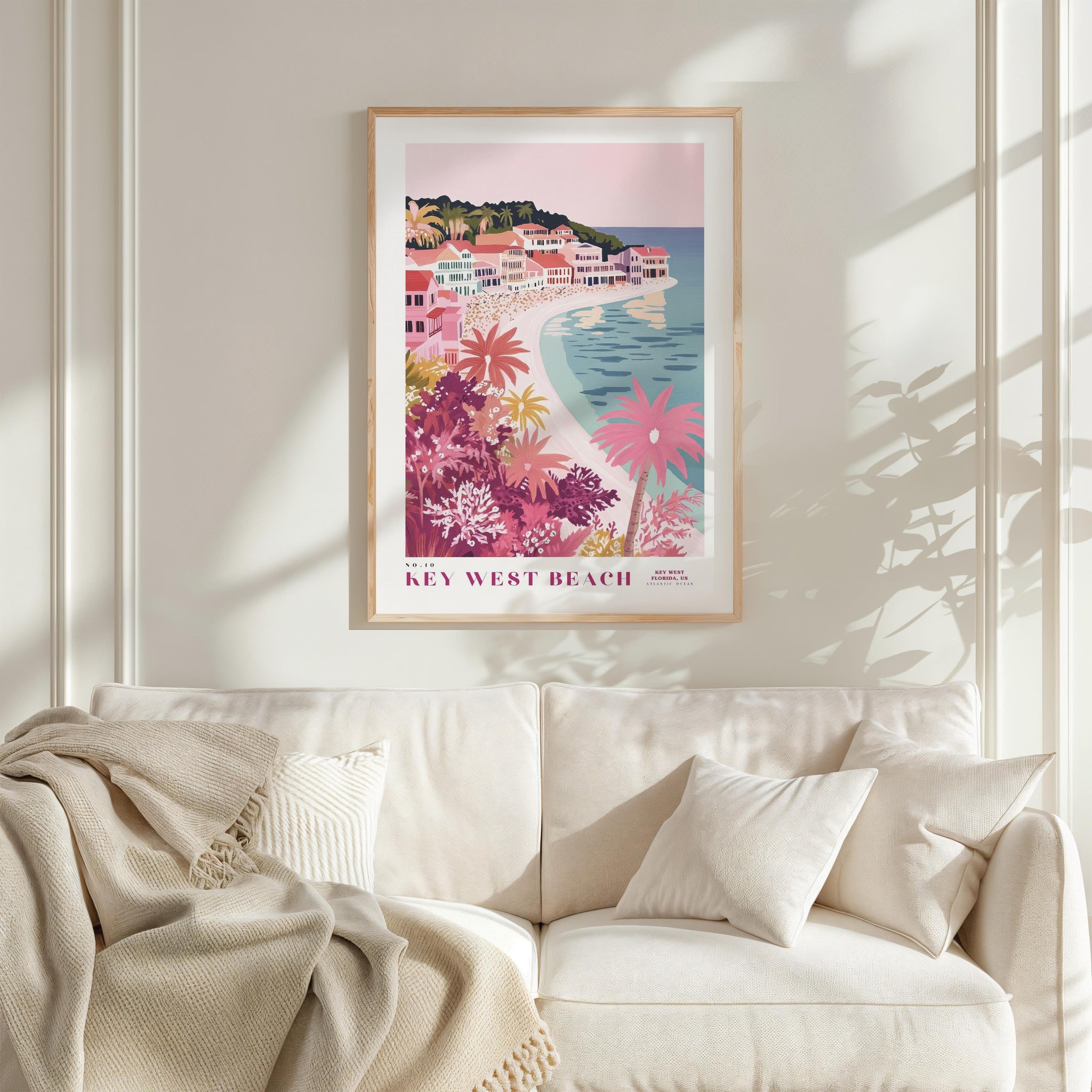 a framed poster of a beach scene with palm trees and colorful buildings, hanging on a wall above a white couch with pillows.