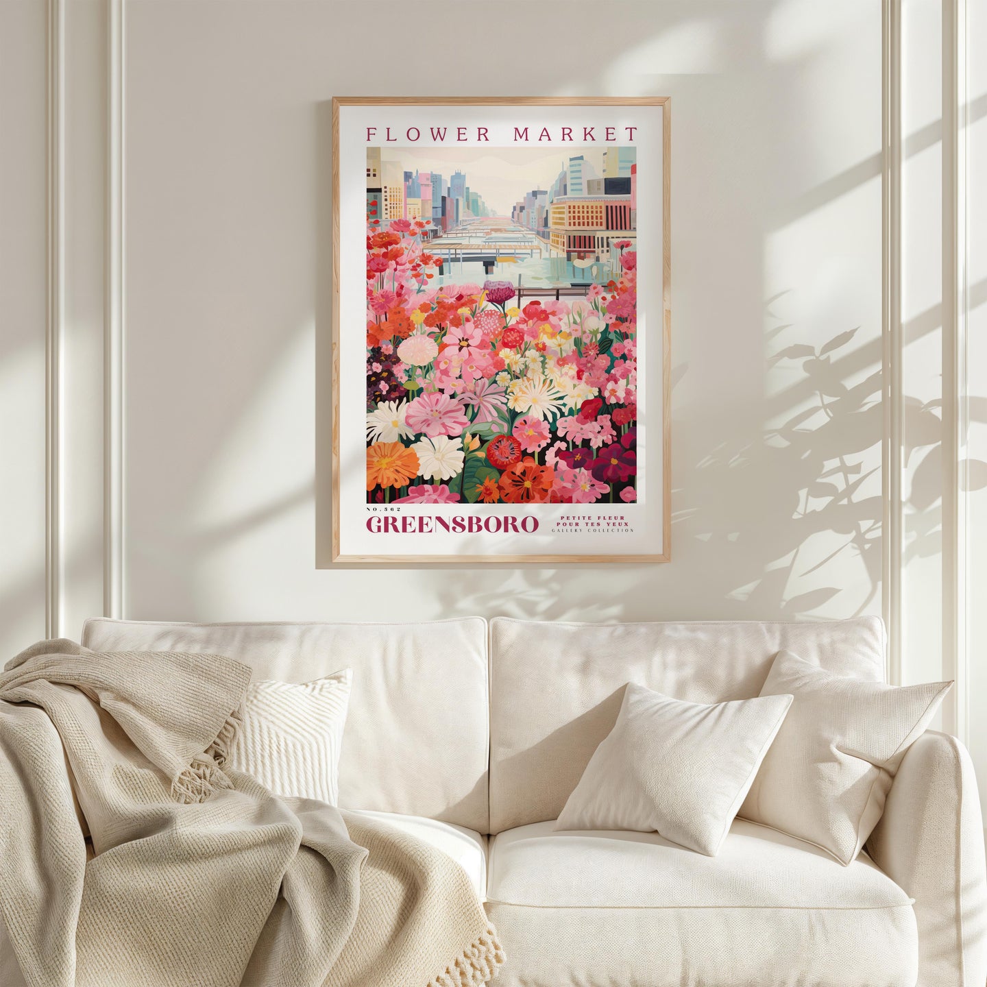 a framed poster of a flower market in Greensboro, North Carolina, hanging on a wall above a white couch.