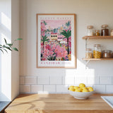 a kitchen scene with a framed poster of a colorful floral market in Zanzibar hanging on the wall above a wooden counter. On the counter, there is a bowl of lemons and a plant.