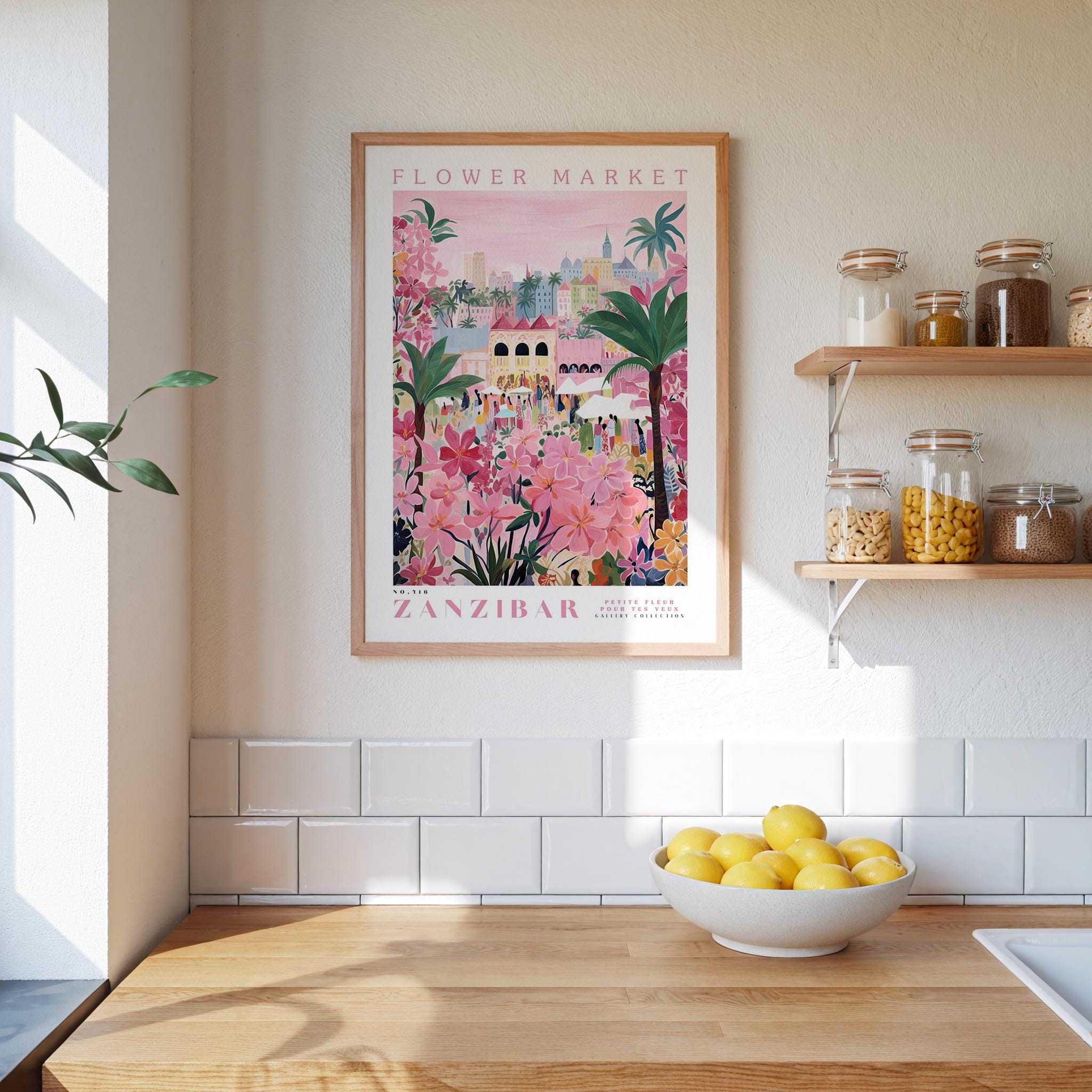 a kitchen scene with a framed poster of a colorful floral market in Zanzibar hanging on the wall above a wooden counter. On the counter, there is a bowl of lemons and a plant.