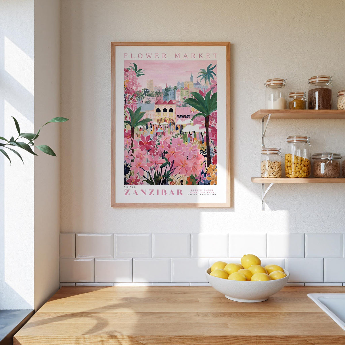 a kitchen scene with a framed poster of a colorful floral market in Zanzibar hanging on the wall above a wooden counter. On the counter, there is a bowl of lemons and a plant.