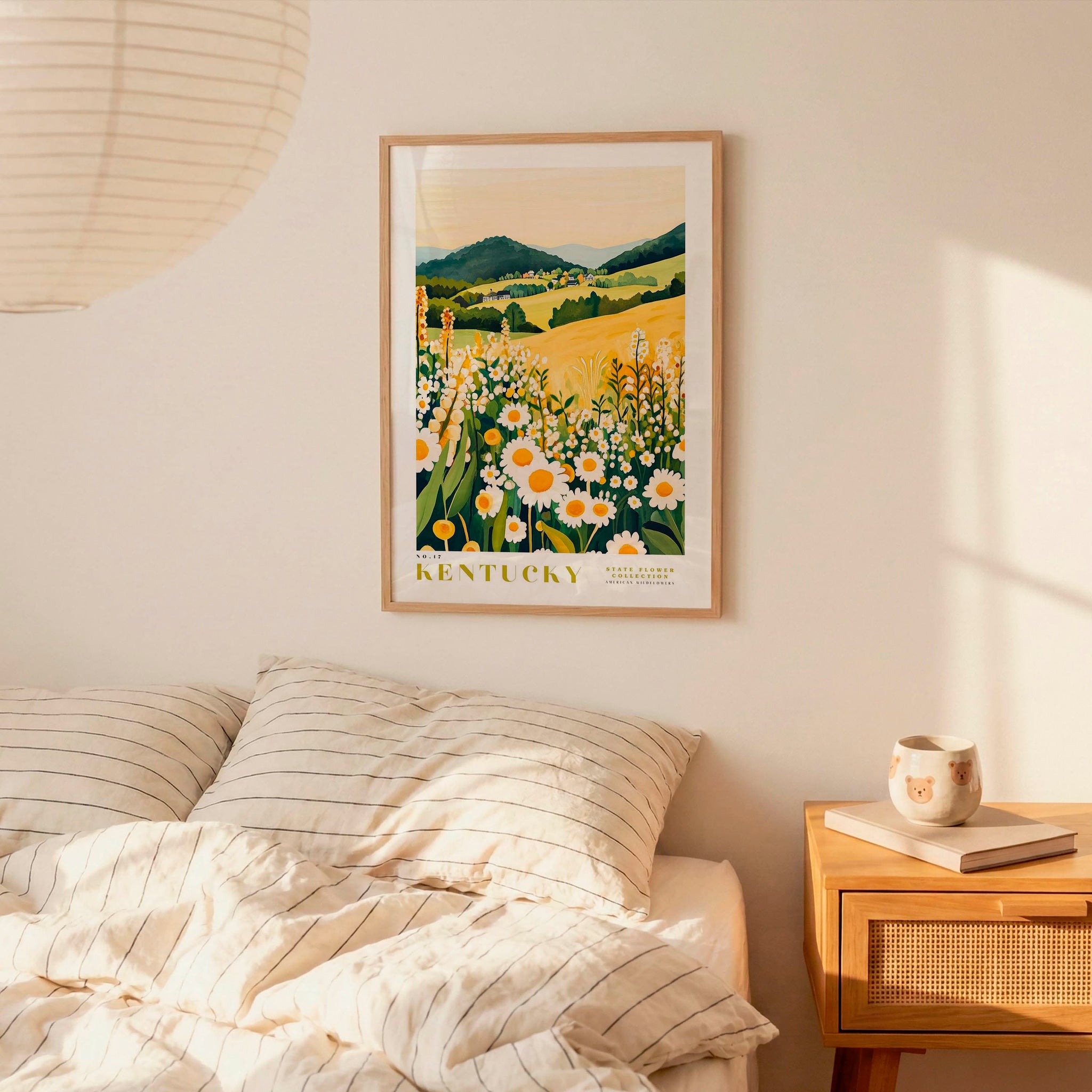 a bedroom scene with a framed poster of a field of flowers hanging on the wall above a bed with striped pillows.
