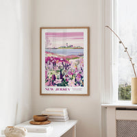 a framed poster of a scenic landscape with a body of water and a small island, hanging on a wall in a room with a window and a table with books and a vase.
