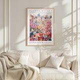 a framed poster of a colorful floral scene hanging on a wall above a white couch with a blanket draped over it.