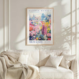 a framed poster of a colorful garden scene hanging on a wall above a white couch with pillows.