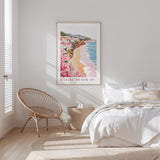 a serene bedroom scene with a bed, a woven chair, and a framed poster of Malibu Beach hanging on the wall.