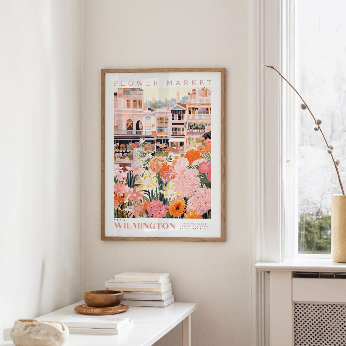 a framed poster of a colorful illustration of a flower market in Wilmington, North Carolina, hanging on a wall.