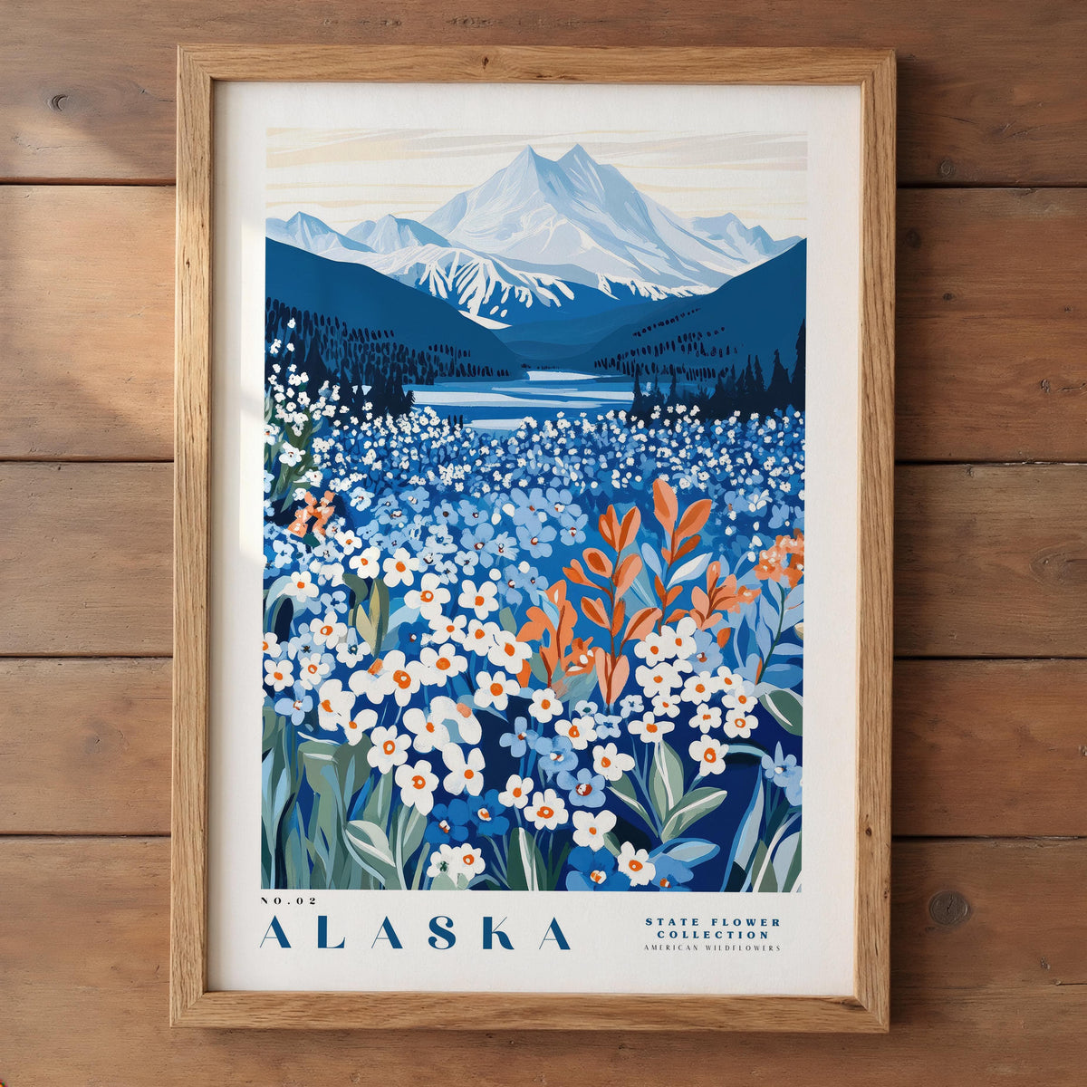The image is a framed poster depicting a scenic landscape of Alaska, featuring a mountain range, a lake, and a field of wildflowers.