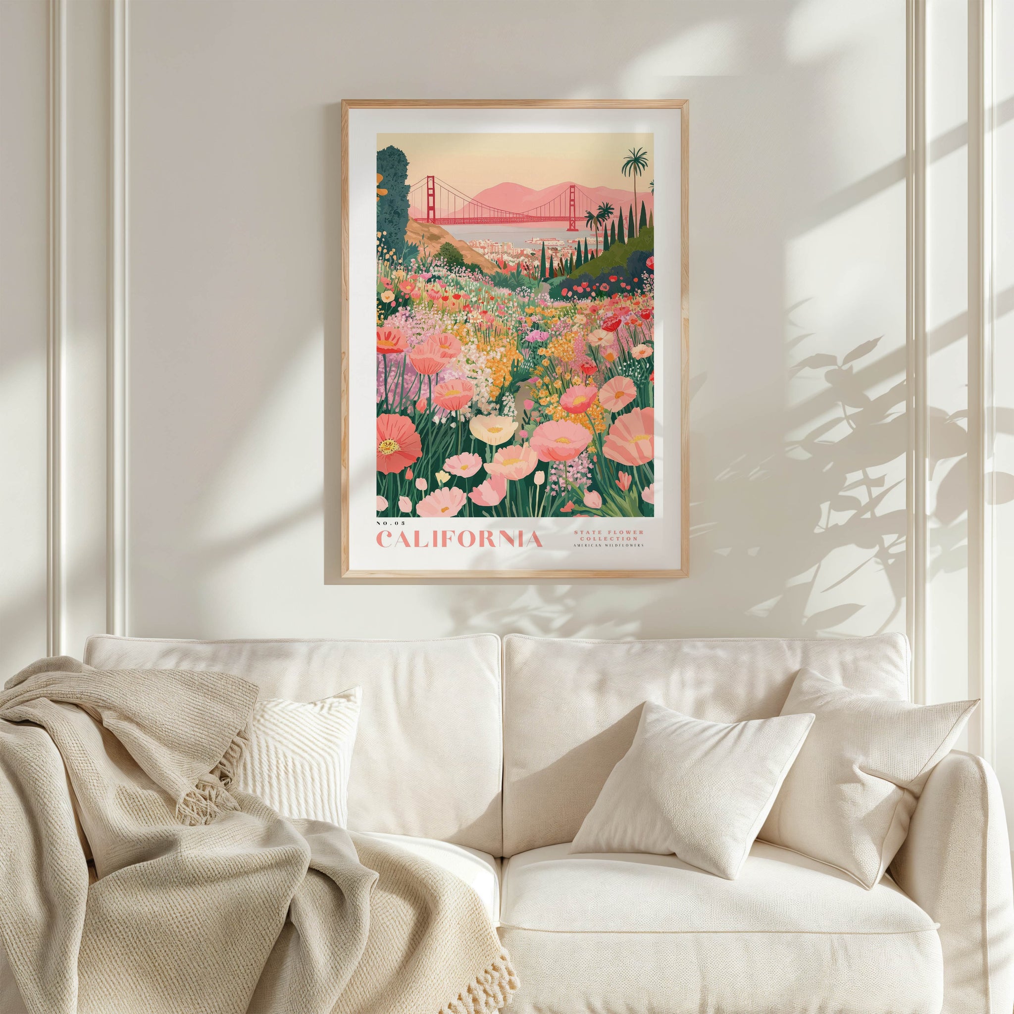 a framed poster of a vibrant garden scene with a bridge in the background, hanging on a wall above a white couch with a blanket draped over it.