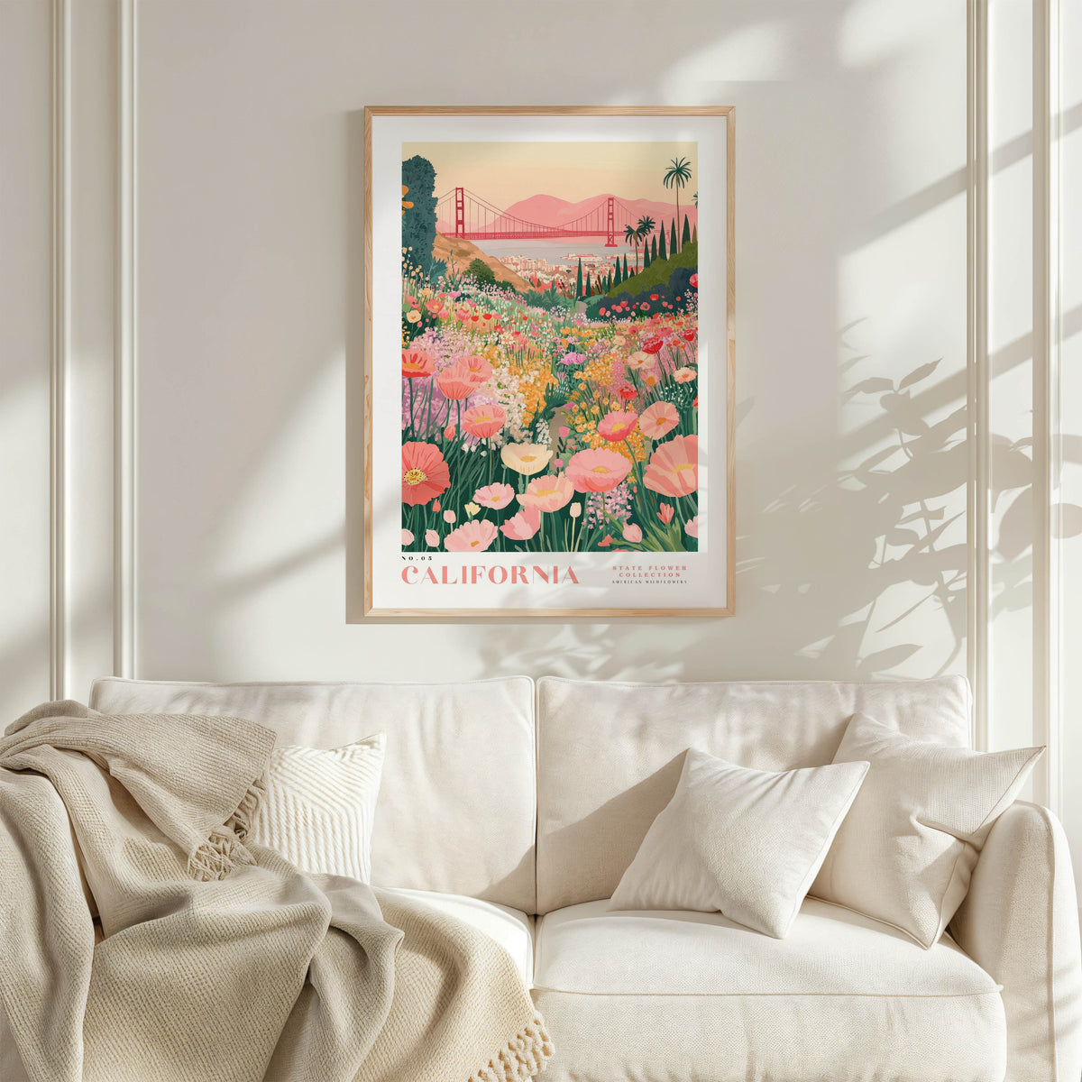 a framed poster of a vibrant garden scene with a bridge in the background, hanging on a wall above a white couch with a blanket draped over it.