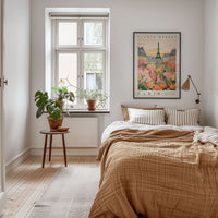 a cozy bedroom with a large bed, a nightstand with a plant, and a framed poster of Paris on the wall.