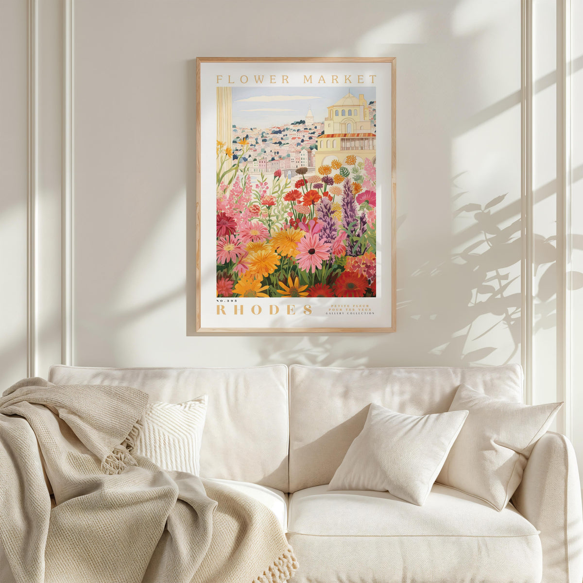 a framed poster of a colorful garden scene hanging on a wall above a white couch with a blanket draped over it.