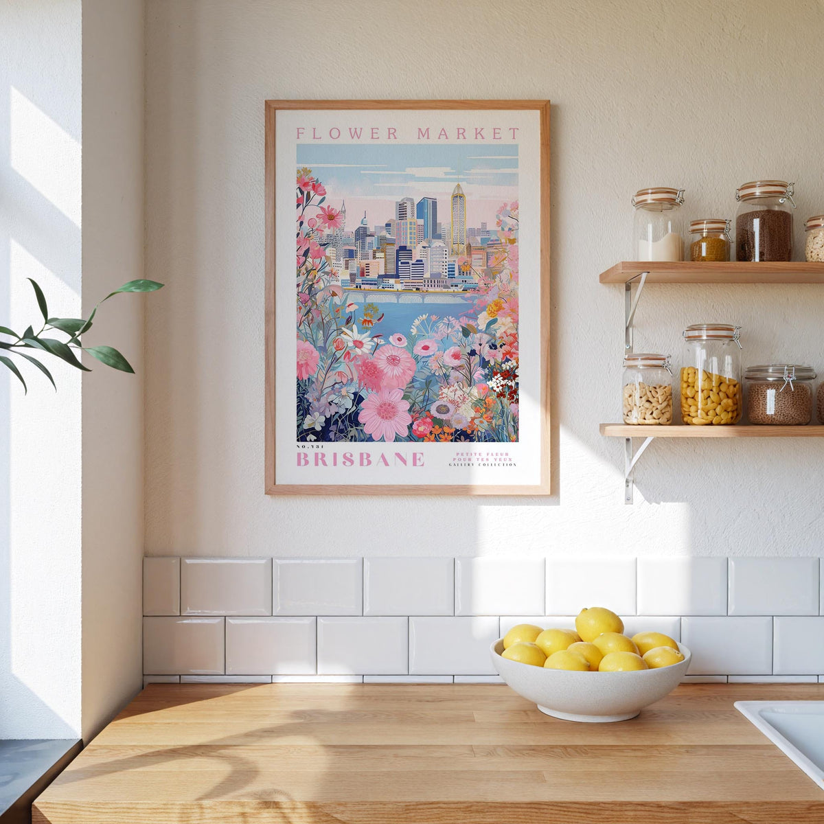 a framed poster of a cityscape with a flower market in the background, hanging on a wall above a wooden counter with a bowl of lemons.