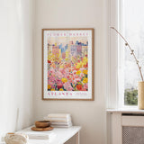 a framed poster of a colorful floral scene hanging on a wall, with a window and a small table with books and a vase in the foreground.