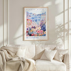 a framed poster of a colorful floral scene hanging on a wall above a white couch with a blanket draped over it.