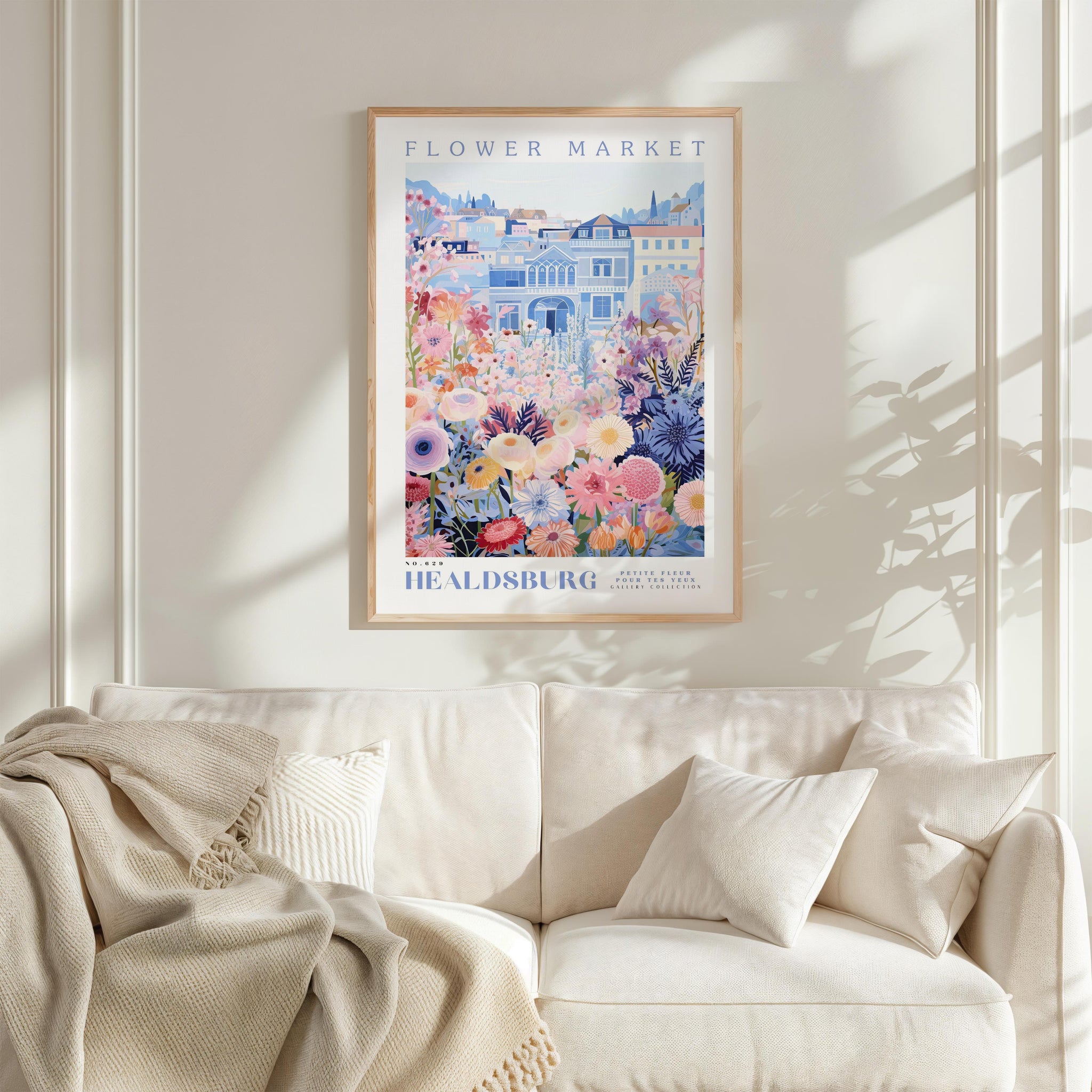 a framed poster of a colorful floral scene hanging on a wall above a white couch with a blanket draped over it.