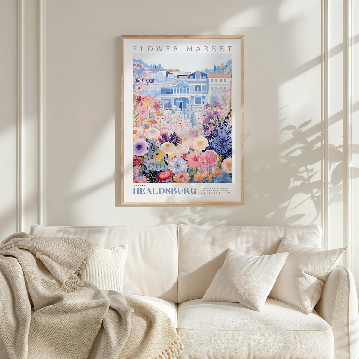 a framed poster of a colorful floral scene hanging on a wall above a white couch with a blanket draped over it.