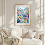 a framed poster of a colorful floral scene hanging on a wall above a white couch with pillows.