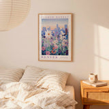 a bedroom scene with a framed poster of a cityscape and flowers hanging on the wall above a bed with striped pillows.