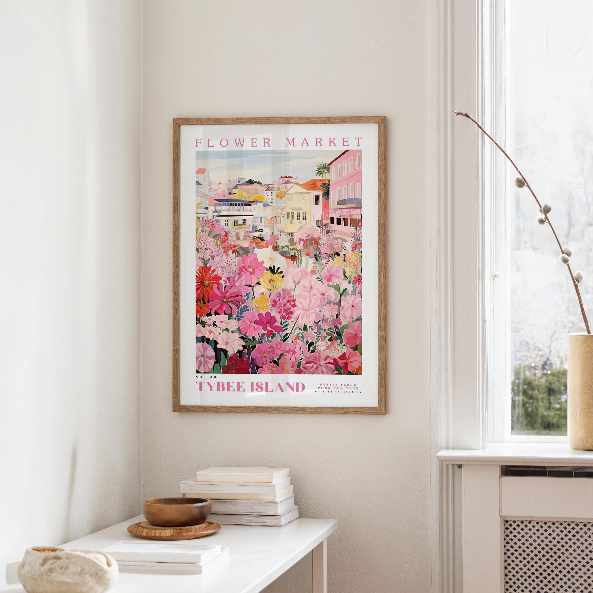 a framed poster of a colorful floral scene hanging on a wall, with a white table and a vase of flowers in the foreground.